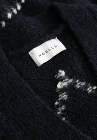 Schwarzes Strickkleid mit weißem Webmuster und einem weißen eingenähten Etikett mit der Aufschrift "NOELLA".