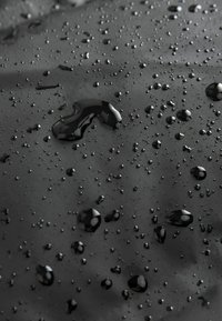 Tejido impermeable negro con una textura suave, que presenta gotas de agua dispersas. La superficie es mate con un leve brillo, lo que resalta su durabilidad.