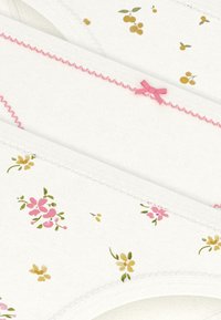 Τρία ζευγάρια γυναικείων εσώρουχων από λευκό βαμβάκι, με λουλουδάτα σχέδια σε ροζ, κίτρινο και πράσινο, με ροζ κορδέλες και κυματιστά τελειώματα.