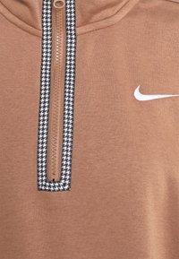 Brun hoodie med en svart och vit houndstooth dragkedja som accent. Har en halvdragkedja-design och en vit Nike-logotyp på bröstet. Mjuk textur.