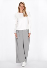 Top lung cu mâneci lungi alb și pantaloni gri largi cu pliuri, asociați cu adidași albi, pe un fundal alb simplu.