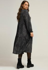 Czarna sukienka w panterkę z długimi rękawami, zebranym talią i warstwowym detalem spódnicy. Noszona z czarnymi botkami za kostkę. Gładka faktura.