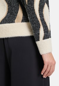 Gebreide trui met een fuzzy textuur, voorzien van abstracte zwarte en beige patronen. De boorden zijn crèmekleurig en geribbeld voor extra structuur.