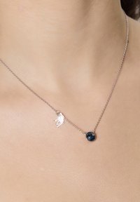 Srebrny naszyjnik z małym charms'em i okrągłym ciemnoniebieskim kamieniem szlachetnym. Łańcuszek jest delikatny o gładkiej teksturze.