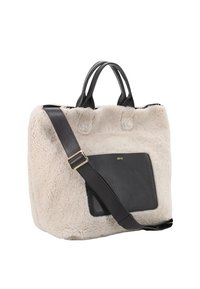 Sac fourre-tout en fausse fourrure crème avec une poche avant en cuir noir et une sangle, dotée de poignées supérieures doubles et d'une texture douce.