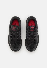 Czarne sportowe sneakersy z siateczki i materiałów syntetycznych, z grubą podeszwą, teksturowanymi akcentami i czerwonymi detalami wewnątrz.