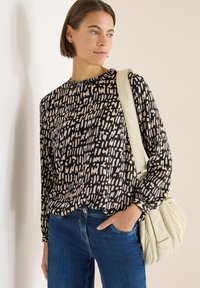 Musta- ja kermaanvärinen pitkähihainen pusero, jossa on abstrakti kuvio, yhdistettynä farkkuihin ja vaalean kermaan väriseen käsilaukkuun. Rentoutunut istuvuus, pehmeä kangas.