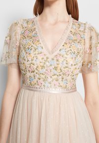 Abito ricamato con scollo a V, maniche a sbuffo trasparenti, motivi floreali in colori pastello e una vita in satin. Il tessuto appare morbido e strutturato.