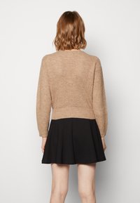 Cardigan en tricot beige à manches longues, avec un motif texturé et une taille ajustée, associé à une jupe noire évasée.