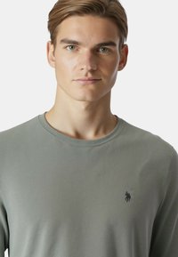 Maglietta a maniche lunghe verde chiaro con trama a coste, con un piccolo logo nero sul petto a sinistra e una classica scollatura tonda.