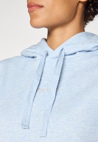 Hoodie blu chiaro con finitura testurizzata, dotato di cordino e piccolo logo ricamato sul petto.