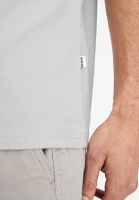 Lys grå t-shirt lavet af blødt stof, med en sideetiket, afslappet pasform og korte ærmer. Nederkanten har dobbeltsyning for holdbarhed.