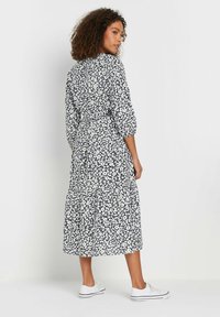 Vestido midi floral en marino con flores blancas, con mangas largas abullonadas, un cinturón en la cintura y una falda con volantes. Llevado con zapatillas blancas.