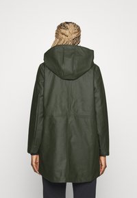 Manteau imperméable long vert olive avec capuche, présentant une texture lisse, des coutures visibles et deux poches latérales.