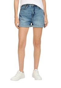 Dżinsowe szorty w jasnoniebieskim odcieniu z podwiniętymi nogawkami i klasycznym pięciopocketowym wzorem, w połączeniu z białymi trampkami.