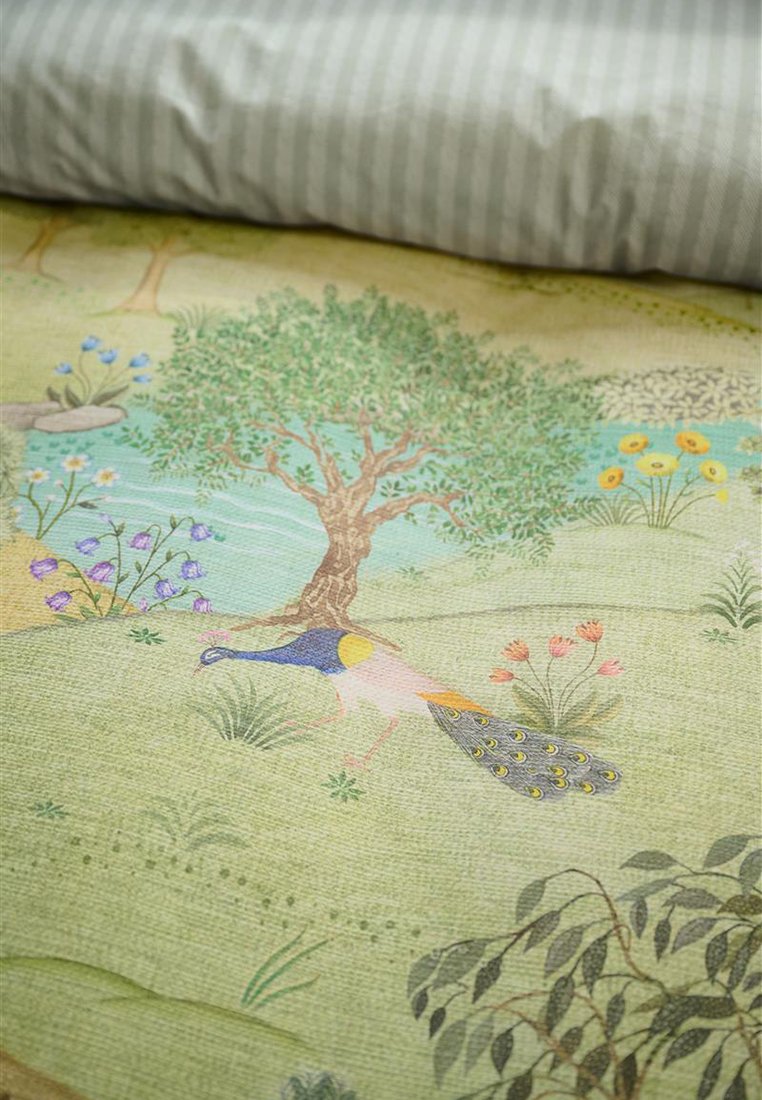 Dekoracyjna tkanina z drzewem, kwiatami i pawiem o kolorowym upierzeniu, na teksturowanym zielonym tle. Widoczna pasiasta szara poduszka.