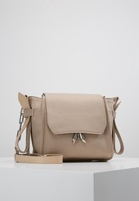 Béžová crossbody taška vyrobená z texturované tkaniny s klopovým uzávěrem, stříbrnou kováním a nastavitelným popruhem. Obsahuje dvojité dekorativní akcenty.