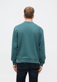 Crewneck sweatshirt i teal, laget av myk stoff. Har ribbestrikkede cuffs og hem, med et enkelt design og avslappet passform. Kombinert med mørke jeans.