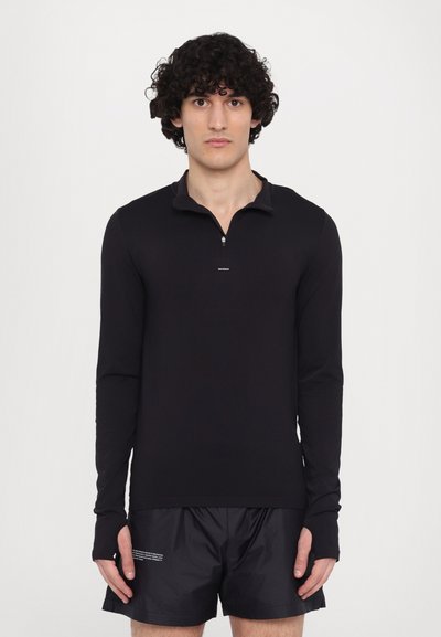 Schwarzes Langarmshirt mit einem halben Reißverschluss am Kragen, aus glattem Stoff. Mit einem Logo auf der Brust und Daumenschlitzen in den Ärmeln.