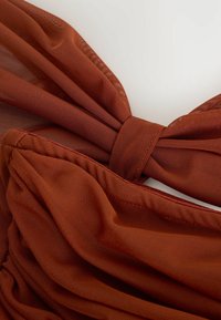 Tessuto di colore ruggine con un design a rete testurizzato, con sezioni arricciate e un dettaglio annodato che crea un aspetto strutturato.