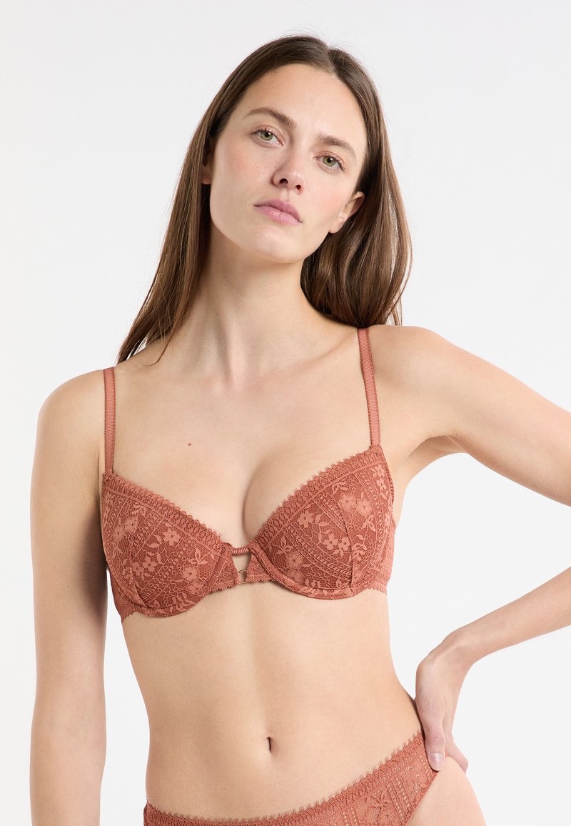 Reggiseno marrone in pizzo con motivo floreale testurizzato, supporto con ferretto, spalline regolabili e dettagli decorativi anteriori.