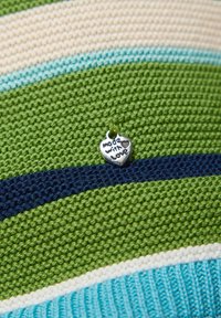 Gestrickter Stoff in Grün, Marine, Creme und Hellblau gestreift, mit einem silbernen herzförmigen Anhänger, auf dem "made with love" eingraviert ist.