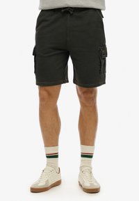 Pantaloni cargo grigio scuro in cotone misto, con vita regolabile e tasche laterali. Abbinati a sneaker bianche e calze a righe.