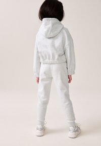 Hellgraue Kapuzenjacke und passende Jogginghose aus weichem Stoff, mit elastischen Bündchen und Kapuze, kombiniert mit weißen und grauen Sneakers.
