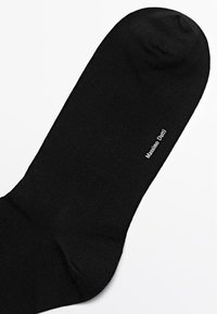 Black cotton sock with a smooth texture, featuring a rounded toe and a white logo "Massimo Dutti" printed near the ankle.