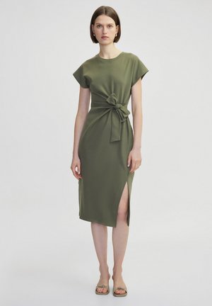 Robe vert olive à manches courtes, détail de nœud à l'avant et fente sur le côté. Tissu lisse et léger, design longueur genou et esthétique minimaliste.