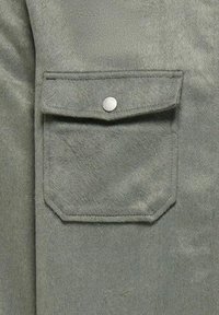 Gray faux suede fabric features a chest pocket with a pointed flap and a silver snap button. The texture appears soft and plush.