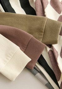 Een close-up van stoffen manchetten in verschillende kleuren: crème, mauve, olijfgroen, zwart en met een patroon, die textuur en ontwerpelementen tonen.