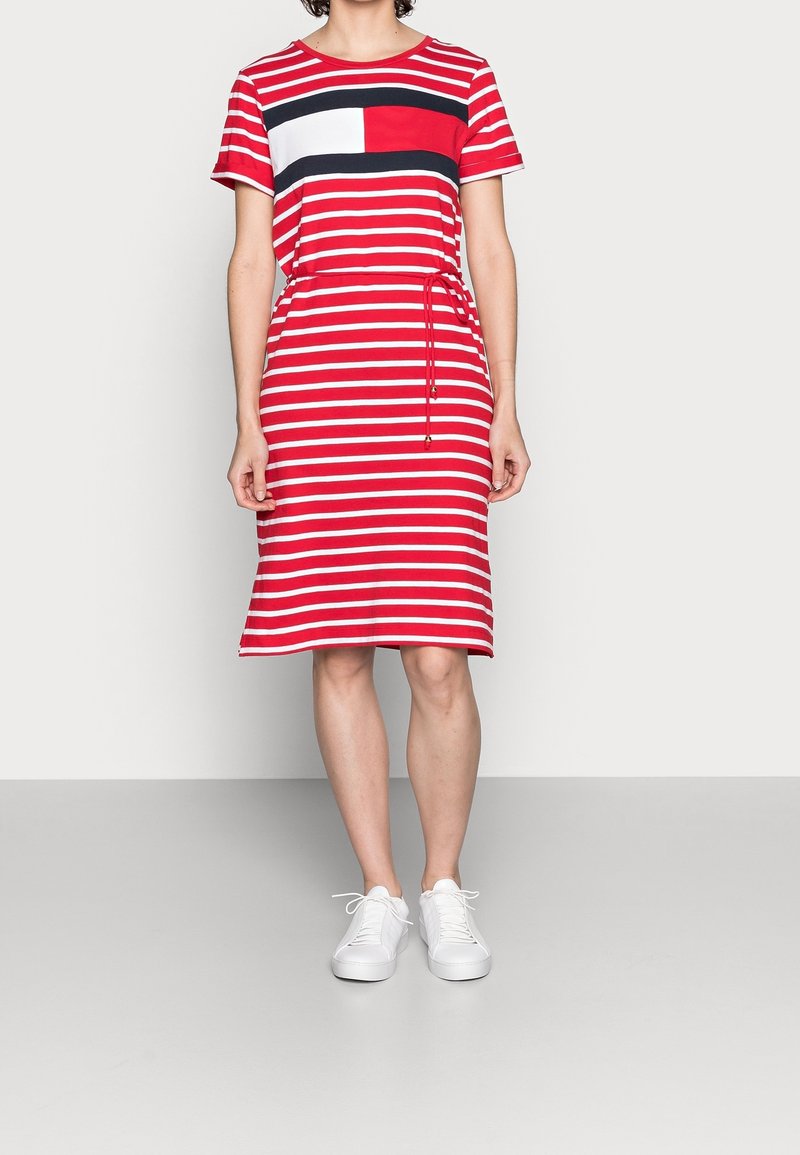 Punainen ja valkoinen raidallinen lyhythihainen mekko, jossa on joustava vyötärö ja tummansiniset värilohkokehykset, yhdistetty valkoisiin tennareihin.