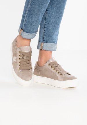 Baskets compensées en daim beige avec détail étoile et lacets épais beiges, portées avec un jean bleu retroussé sur un fond blanc.