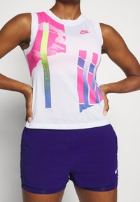 Top senza maniche Nike in tessuto mesh bianco, con vivaci strisce grafiche rosa, verde e blu. Abbinato a pantaloni sportivi viola.