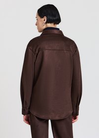 Braunes, elegantes Hemd mit glatter Textur, geknöpften Manschetten und Kragen. Die Rückseite ist mit einem Passe-Detail und einem lockeren Schnitt versehen.