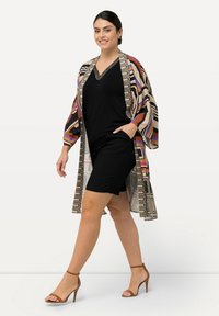 Vícebarevná vzorovaná kimono bunda přes černé šaty, s výstřihem do V, kapsami a sandály na kotníky. Hladká textura látky.