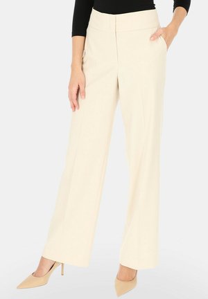 Kobieta nosząca kremowe, szerokie spodnie z wysokim stanem i bocznymi kieszeniami oraz beżowe wysokie szpilki z szpiczastym noskiem, w połączeniu z czarnym topem.