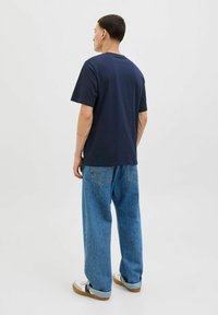 Tamsiai mėlynas medvilninis marškinėliai su apvaliu kaklu, trumpomis rankovėmis; derinami su šviesiai mėlynais plačiais džinsais ir baltais sportbačiais su mėlynais akcentais.