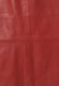 Tela de cuero rojo con una textura suave, con una costura hecha verticalmente en el centro, mostrando un color sólido sin patrones.