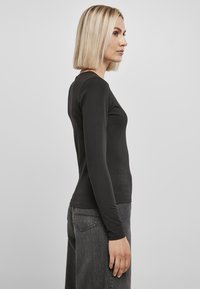 Sort langærmet top, tætsiddende design med rund hals, lavet af glat stof, parret med løse mørkegrå jeans. Enkel og minimalistisk stil.