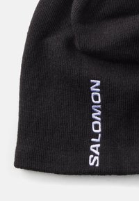 Gorro de punto negro con una textura suave. Presenta la palabra "SALOMON" bordada en púrpura claro en un lado.