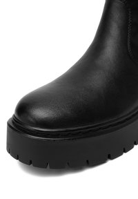 Melna ādas potītes zābaks ar noapaļotu purngalu, biezam platformas zolei un teksturētu virsmu. Viena slāņa šuvju detaļa ap augšējo malu.