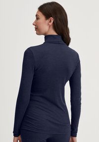 Marineblauwe langemouwen turtleneck top, gemaakt van een zachte, rekbare stof; het aansluitende ontwerp accentueert de silhouet met minimale naden.
