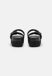 Black platform sandals featuring a smooth synthetic upper, adjustable straps with buckles, and a textured sole for grip.