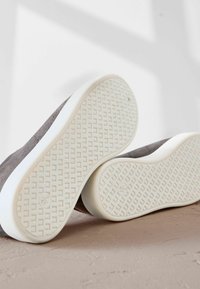 Gray fabric sneakers with white rubber soles. The soles feature a textured grip pattern and the shoes have minimalist design with subtle stitching.