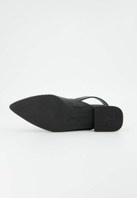 Scarpa nera con tacco alto e punta affusolata, apertura sul retro e tacco piatto. La suola presenta una superficie testurizzata con un logo, evidenziando un design elegante.