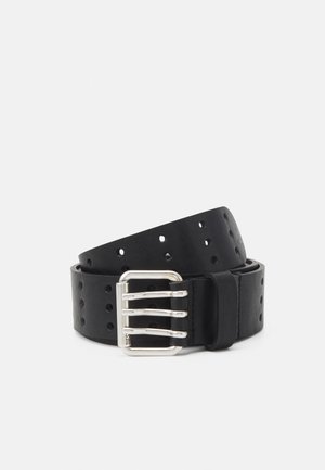 Ceinture en cuir noir avec plusieurs trous ronds et une boucle en métal argenté à triple ardillon, enroulée sur un fond clair uni.