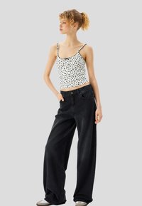 Hvid top med sort blomsterprint og blondekant, sammen med høj talje, vide sorte jeans og grå sneakers.