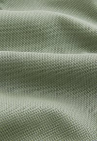 Texturiertes, hellgrünes Gewebe mit einem geometrischen Muster, das ein weiches, gewebtes Material in einer zerknitterten Anordnung zeigt.